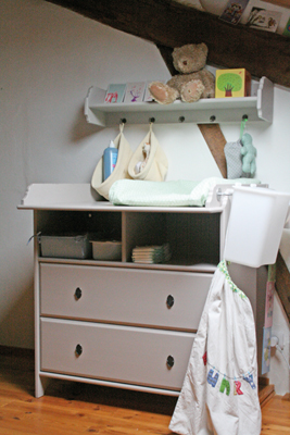 Cette commode table à langer est complétée d’une étagère murale à laquelle sont suspendues des corbeilles de rangement. Très fonctionnel, ce type de modèle nécessite de l’espace mais s’avère très pratique pour garder le linge de bébé à portée de main.  